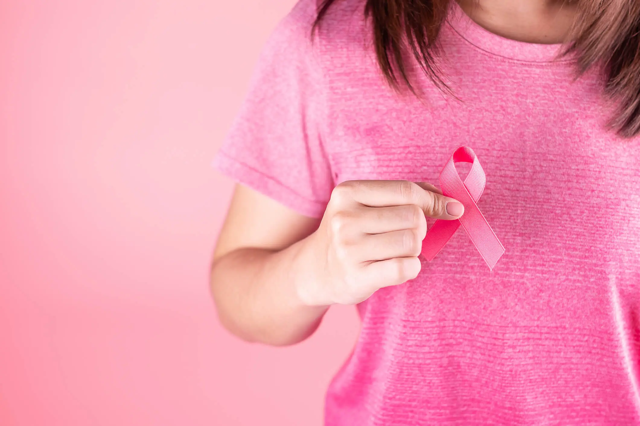 Hand holding a pink awareness ribbon.