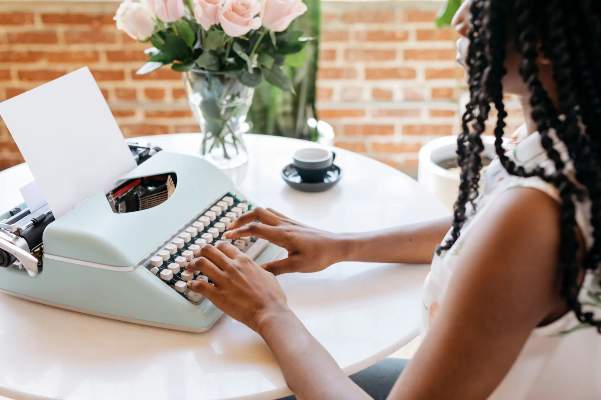 Woman typing on vintage typewriter, brick background.