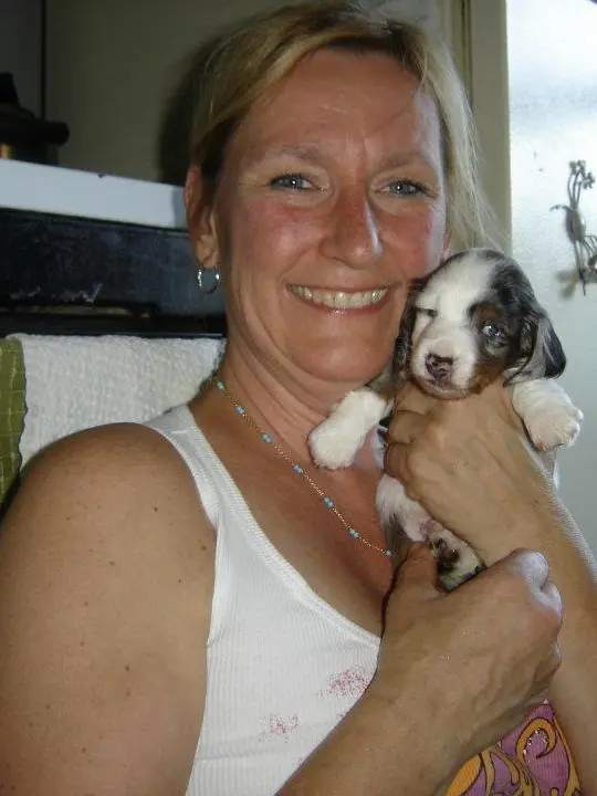 Smiling woman holding a small puppy indoors.