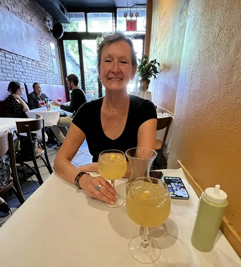 Woman smiling with two drinks at a café table.