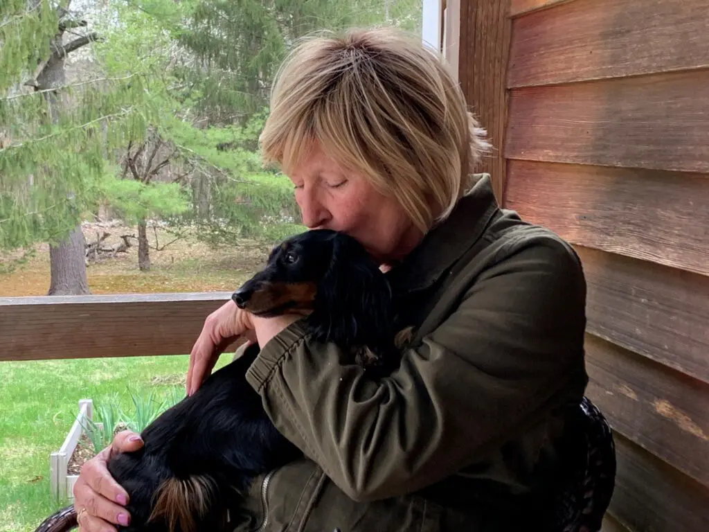 A person lovingly hugging a black dog on a porch.