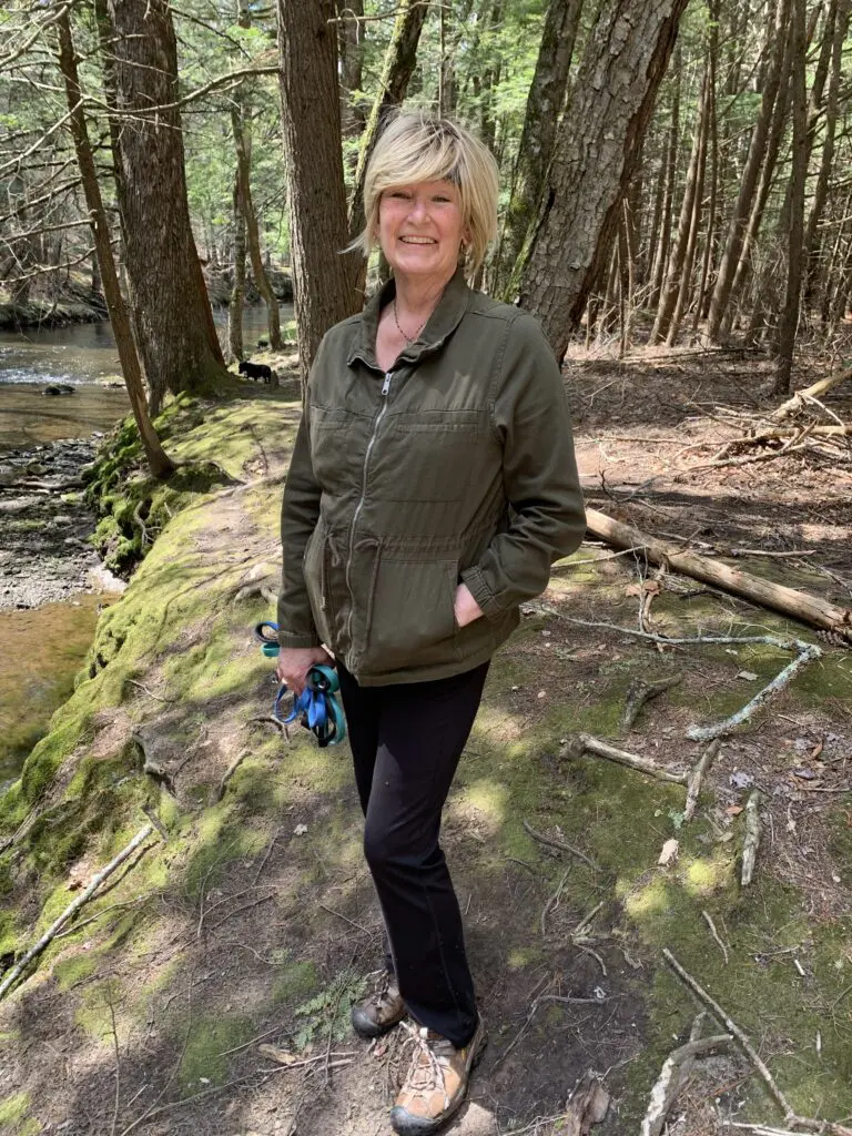 Woman standing on a mossy log in a forest by a creek.